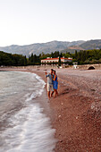 Couple at beach in evening light, Villa Milocer in background, Aman Sveti Stefan, Sveti Stefan, Budva, Montenegro