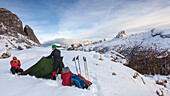 Junges Paar baut ein Zelt im Schnee auf, Dolomiten, Belluno, Venetien, Italien