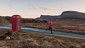 Young woman jogging, passing a red booth, Isle of Skye, Trotternish Peninsula, Scotland, United Kingdom