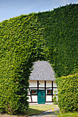 Half-timbered house behind a gate in a hedge of beeches, Monschau-Hoefen, Eifelsteig hiking trail, Eifel, North Rhine-Westphalia, Germany