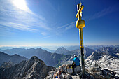 Person sitting beside summit cross of mount Zugspitze, Wetterstein mountain range, Upper Bavaria, Bavaria, Germany