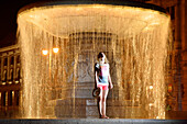 Young woman in front of fountain Wittelsbacherbrunnen at night, Lenbachplatz, Upper Bavaria, Bavaria, Germany