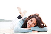 Pretty brunette woman lying on a seaside pier smiling at camera