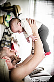Bearded Father with Tattoo Holding-up Infant Son Above his Head, Indoor