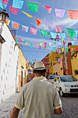 'Mexico, Guanajuato, Man Walking Under Colorful Street Decorations; San Miguel De Allende'