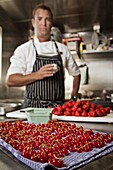 Pastry chef holding a cup of espresso while standing in kitchen with assorted berries being prepped on counter