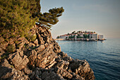 schroffe Felsküste und der Blick zur Luxus Hotel Insel Sveti Stefan, Adria Mittelmeerküste, Montenegro, Balkan Halbinsel, Europa