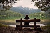 junge Frau sitzt auf Bank und blickt über den Schwarzen See (Crno jezero) im Durmitor National Park, Zabljak, Montenegro, Balkan Halbinsel, Europa