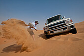 Man trying to dig out 4 wheel drive stuck in soft sand, Liwa, Abu Dhabi, UAE
