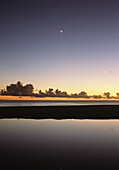 Looking over shallow pool at dusk to moon setting off West coast, Barbados