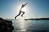 Man jumping off rocks into sea beside Cala Bassa Beach, Ibiza, Spain