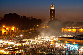 Food stalls in Djemaa El Fna with Koutoubia minaret in background at dusk, Marrakesh, Morocco