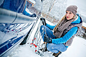 Woman applying chain to tire in snow, Styria, Austria