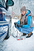 Woman applying chain to tire in snow, Styria, Austria