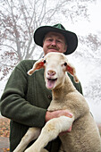 Shepherd Alfred Eichhorn of Eichhorn sheep farm holding a lamb, Schernfeld, near Eichstaett, Altmuehltal, Franconia, Bavaria, Germany