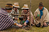 Chagra cowboys with Mountain roses in the bands of their hats cooking trout over a fire at a hacienda during the annual overnight cattle round-up, Andes Mountains, Ecuador