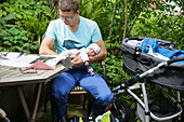 Father holding new born daughter on arm while reading a newspaper, Leipzig, Saxony, Germany