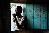 Mann steht am Fenster seiner hütte gelehnt, Uganda, Afrika