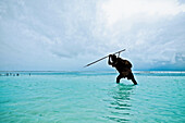 Ein Fischer mit Harpune im seichten Wasser vor der Küste Sansibars, Tansania, Afrika