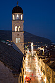 Blick von der Stadtmauer auf Fußgänger in der Stradun Hauptgasse der Altstadt mit Kirchturm von Franziskanerkloster in der Abenddämmerung, Dubrovnik, Dalmatien, Kroatien, Europa