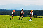 Three children in traditional bavarian dress playing football, Jasberg, Dietramszell, Upper Bavaria, Bavaria, Germany
