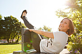 Frau sitzt auf einer Parkbank, Beine über der Lehne, München, Bayern, Deutschland