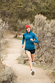 A woman in bright colors jogging on a dirt trail Terrebone, Oregon, USA