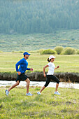 An athletic couple trail running through a field next to a river South Lake Tahoe, California, USA