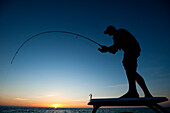 A man fishing in Florida is silhouetted against a sunset Key West, Florida, USA
