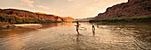 Three women playing and hula hooping in a shallow river at sunset Moab, Utah, USA