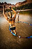 A women with a tattoo plays and hula hoops with a friend in a shallow river Moab, Utah, USA