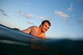A smiling male surfer on his board in the water at sunset in Baja, Mexico Baja, Mexico