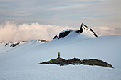 A climber stands on a rock outcrop in the middle of a glacier while climbing in the North Cascades, WA Washington, USA