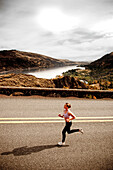 An athletic woman jogging along a deserted road on a beautiful fall day with the Columbia River Gorge in the distance Hood River, Oregon, USA