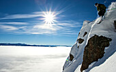 A man skiing off a rock in Jackson Hole, Wyoming with a cloud-filled valley below Jackson, Wyoming, USA