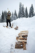 A man chops wood in his snowboarding gear in the snowy backcountry Idaho, USA