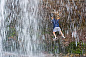 A young girl slides her way along an edge behind a waterfall Alberta, Canada