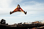 A man does a toe touch jump from a drift log at Rialto Beach, Washington Forks, Washington, USA