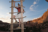 A man climbing a wooden ladder while hiking along a sandstone trail, Canyonlands National Park, Utah Monticello, Utah, USA
