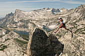 A woman jumping onto a summit in the Enchantment Peaks, Alpine Lakes Wilderness, Leavenworth, Washington Leavenworth, Washington, USA