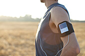Runner in his late 20's wears an MP3 player on his arm while running in an open field in San Diego, California San Diego, California, USA