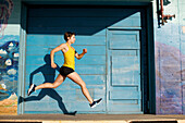 Woman runs and leaps in front of a big blue door in San Diego, California San Diego, California, USA