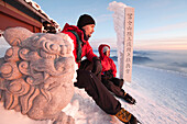 Two people are resting on the summit rim of Mount Fuji, Honshu, Japan next to a traditional Japanese sculpture Honshu, Japan