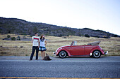 Young couple stand on the road by their broken retro car and try to hitchhike Julian, California, USA