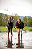Two young women hold hands after a water fight in a large puddle Sandpoint, Idaho, USA