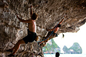 A group of male climbers climbing a severely overhanging wall on the beach in Thailand Hat Tonsai, Krabi, Thailand