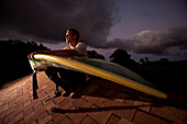 Portrait of a man on a roof with a waveski at sunset Ha'iku, Hawaii, USA