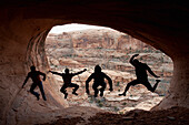 Four young men jumping are silloutted against the mouth of a cave in Moab, UT Moab, Utah, USA