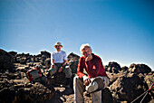 Two senior men have a rest on some small volcanic boulders after a long trek to the summit of Mt. Kilimanjaro Tanzania