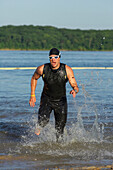 A male athelete running out of the water while training for a triathlon Lawrence, Kansas, USA